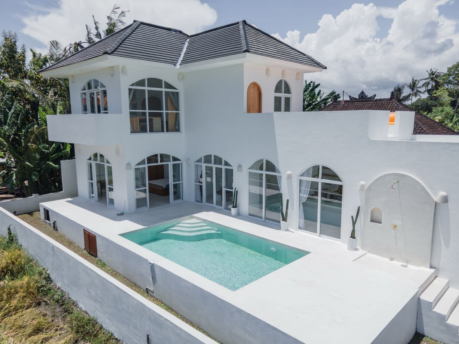 Modern white villa with pool and tropical surroundings.