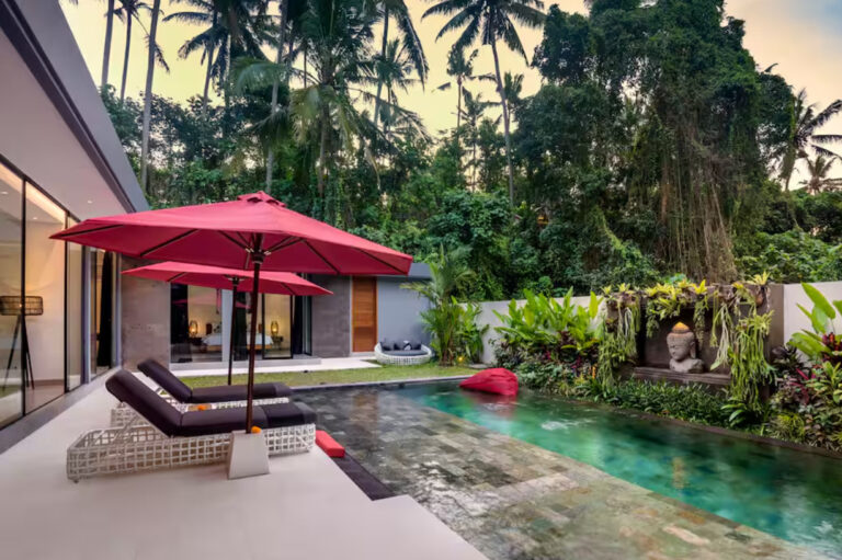 Luxury villa pool with tropical garden and red umbrellas.