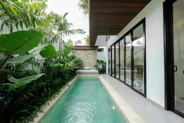 Modern poolside with lush green plants and seating.